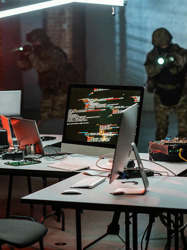 computer desk with PCBA boards multiple computer monitors. computer cables and military in the background. 